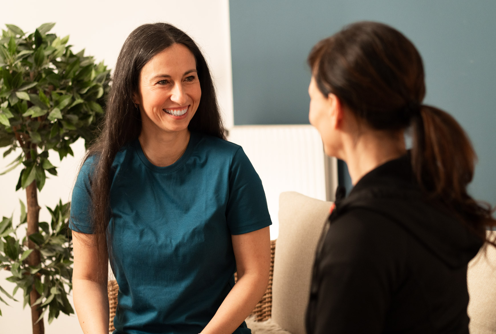 Eine Therapeutin und eine Patientin sitzen sich gegenüber und sprechen in freundlicher Atmosphäre in einem hellen Behandlungsraum.